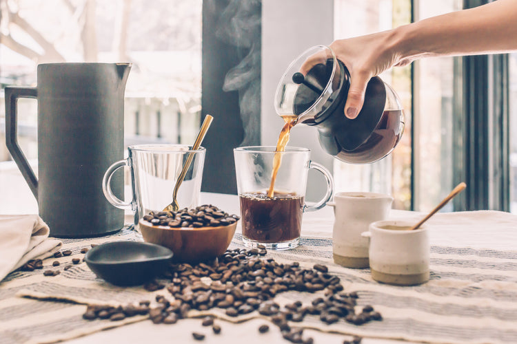 Koffie uitschenken in een glas. Op de voorgrond koffiebonen.