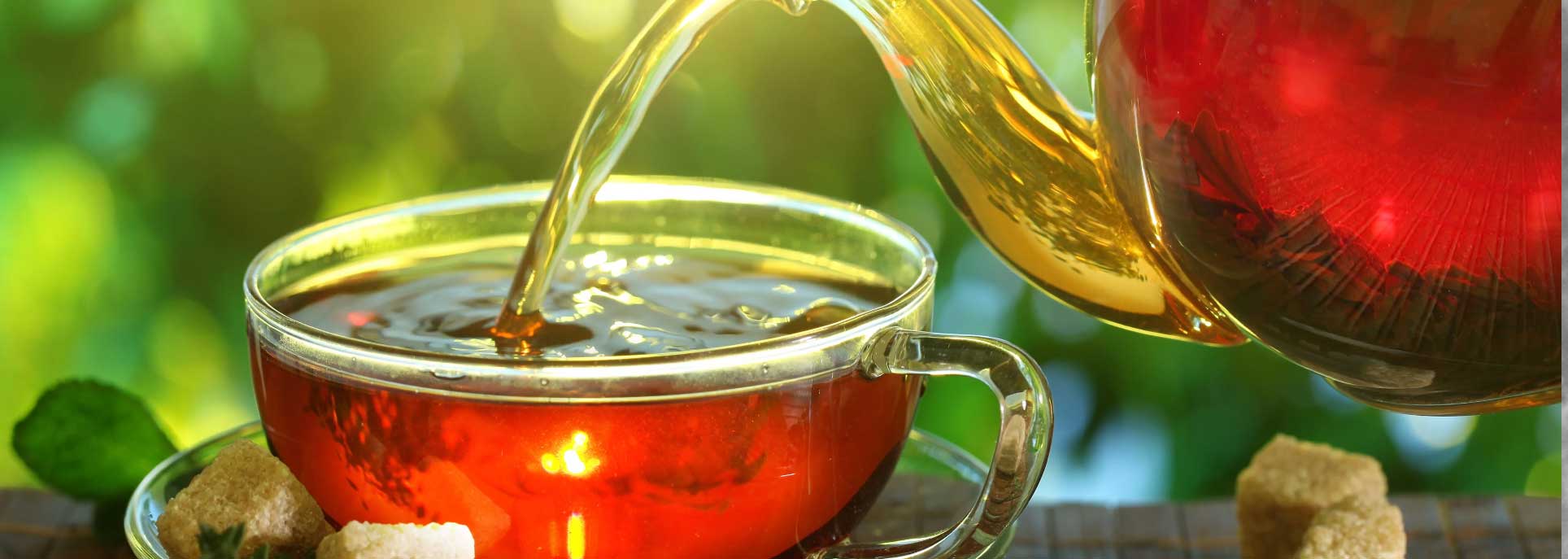 Twinings black tea being poured from a glass teapot into a glass teacup.