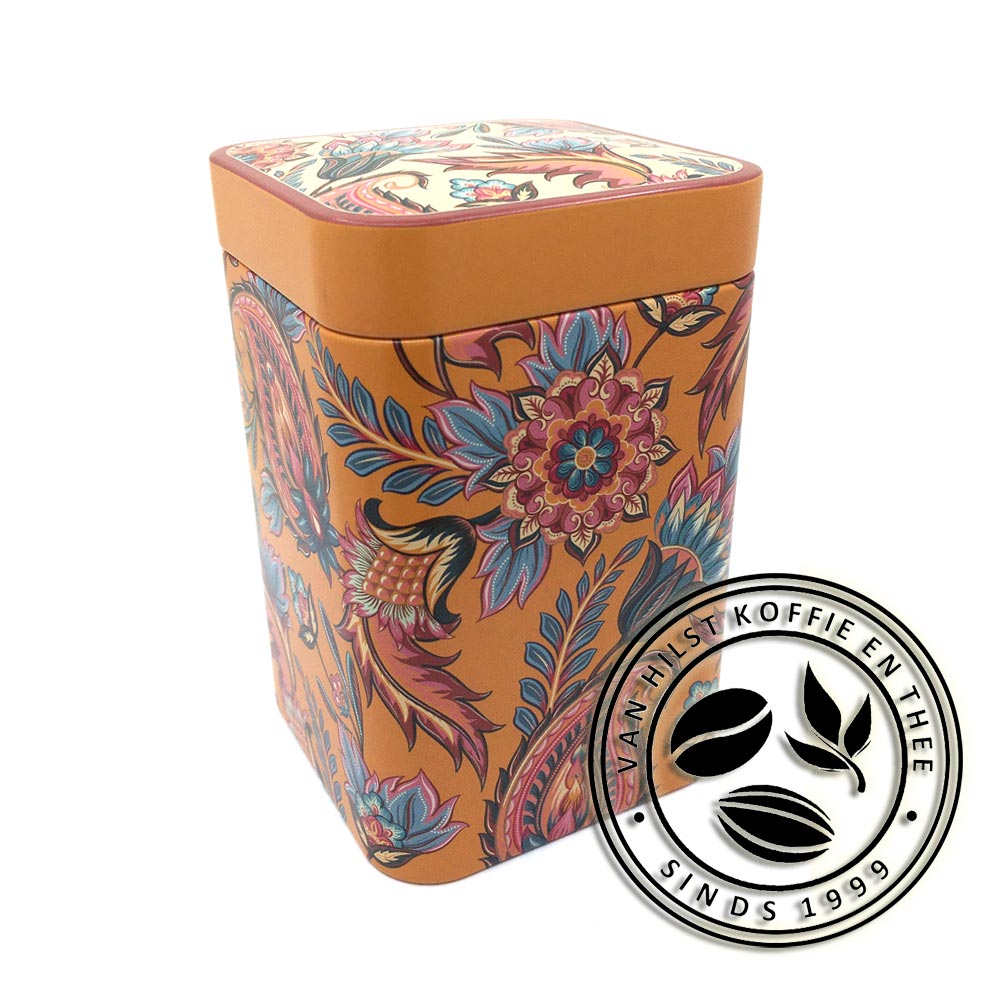 Blikje voor 100 gram thee met paisley motief. Achtergrondkleur van het blik is oranje, de motieven hebben de kleuren oranje, rood, roze, creme en blauw. Het deksel heeft aan de zijkanten dezelfde oranje kleur. De achtergrondkleur van het motief bovenop het deksel is creme.