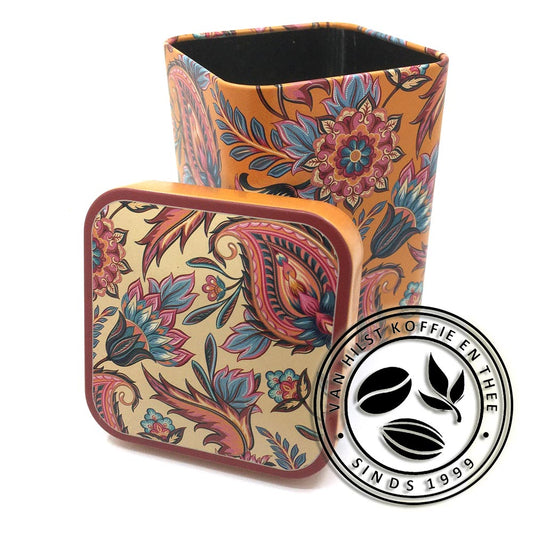 Oranje blikje met paisley motief in de kleuren rood, roze, oranje en blauw. Blikje is open en het deksel leunt er tegenaan. Het deksel heeft dezelfde kleurstelling als het blikje en dezelfde paisley motieven met een creme kleur op de achtergrond. Het blikje is vierkant met afgeronde hoeken, het deksel is iets bol.