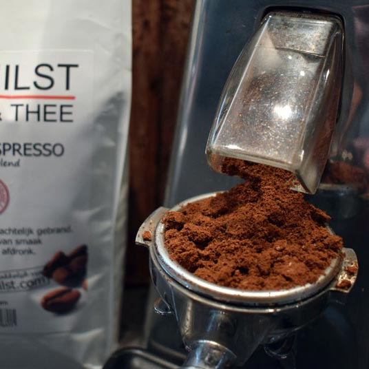 Gemalen koffie (Milano Espresso) die vers uit de maalmolen in de filterdrager van de espressomachine valt.