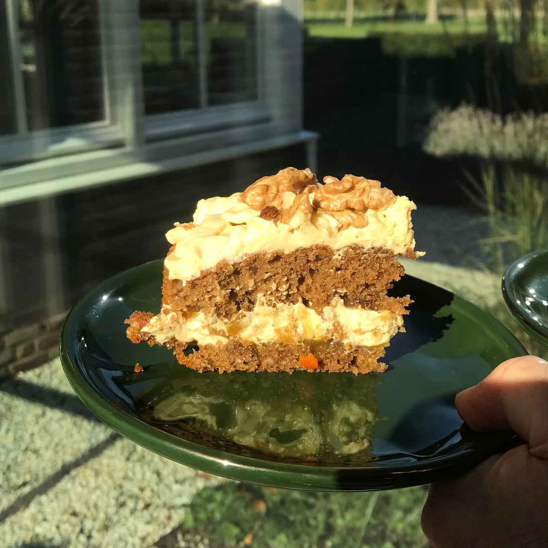 Een punt Koffiecake met walnoten op een groen bordje. Je ziet de laagjes cake, afgewisseld met mokkacreme en walnoten erbovenop. 
