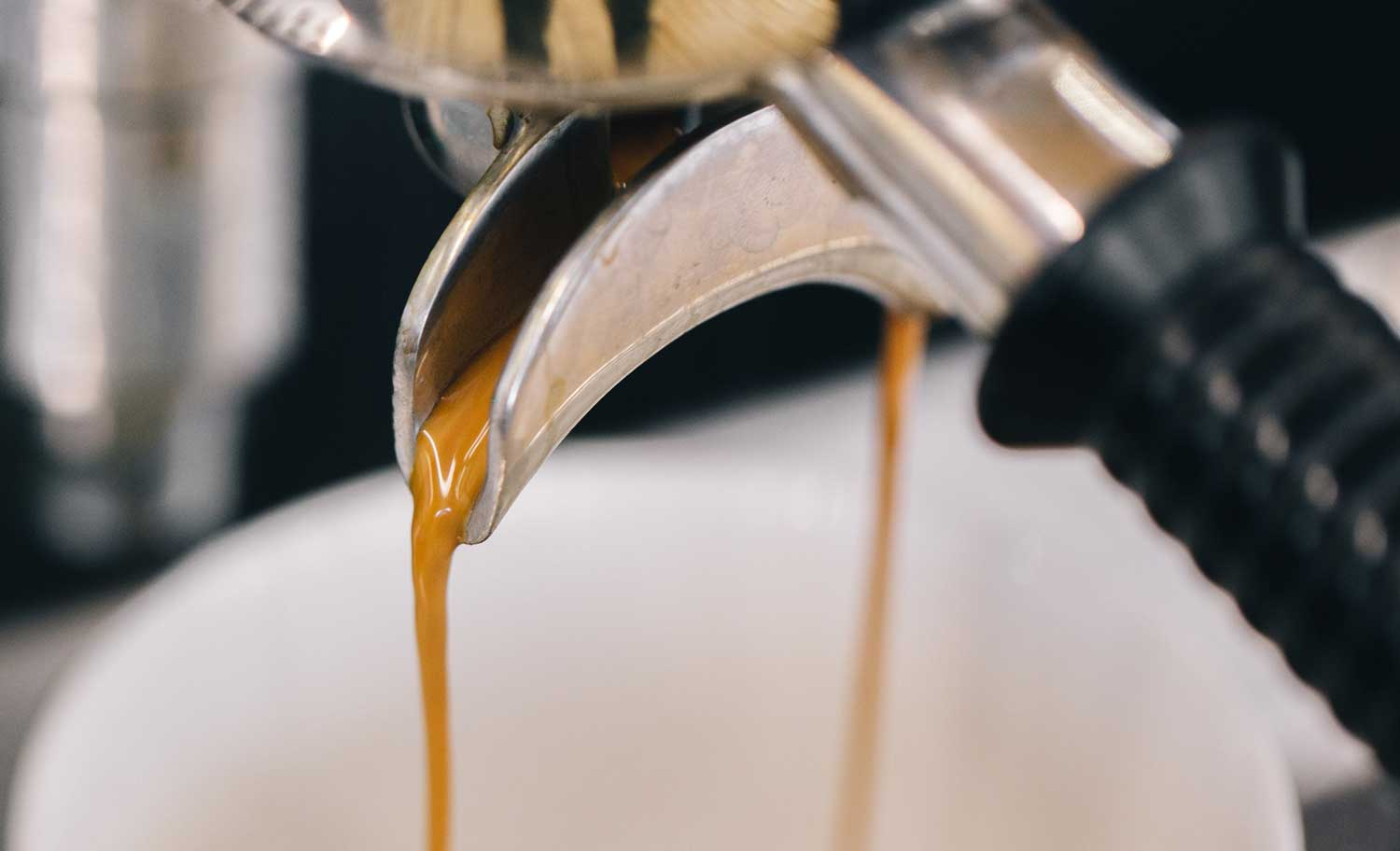Closeup van koffie die uit de piston van een espressomachine loopt.